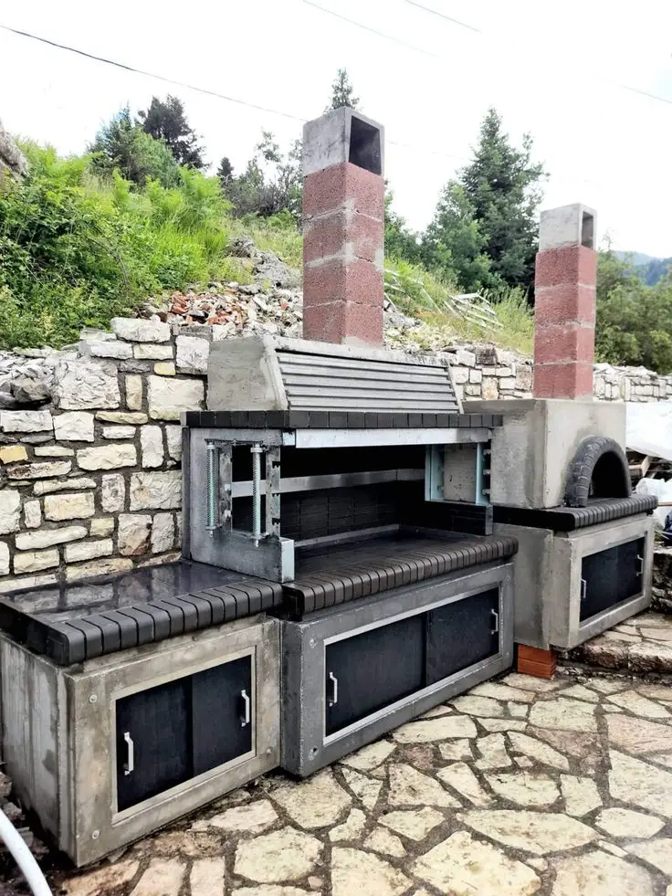 Outdoor barbecue grill and pizza oven combination with stone and brick design, featuring dual chimneys and built-in storage cabinets.