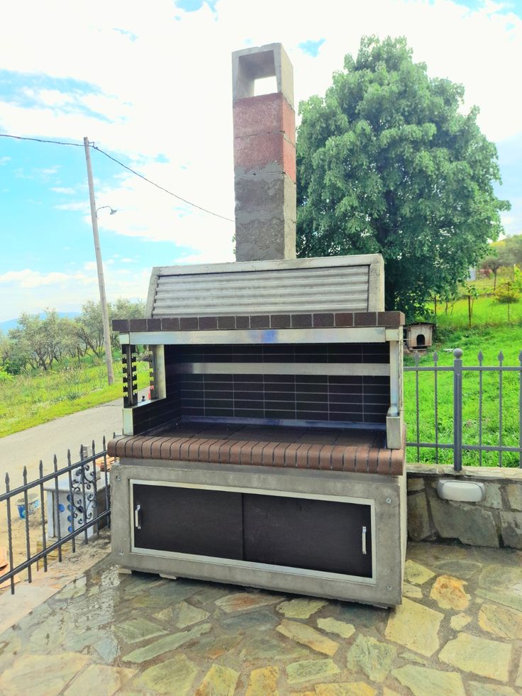 Compact outdoor barbecue grill with a chimney, designed with a sleek stone finish and ample cooking space, set on a tiled patio.