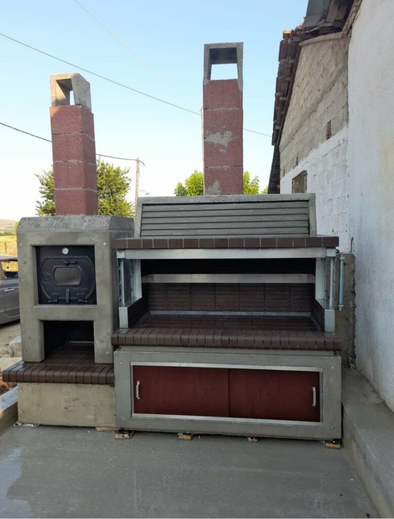 Outdoor barbecue station with a built-in pizza oven and dual chimneys, featuring a rustic tiled design and storage cabinets.