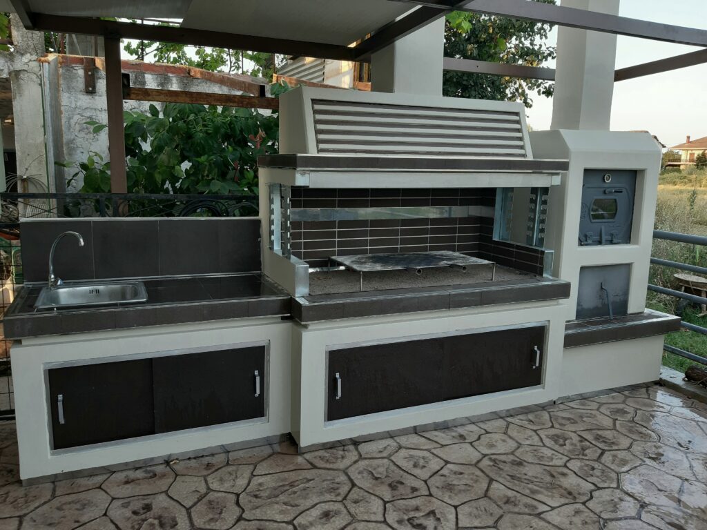 Modern outdoor kitchen setup featuring a built-in wood-fired pizza oven, barbecue grill, sink, and storage compartments.